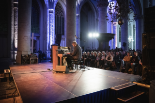 Man speelt in een kerk een piano op een podium voor publiek 